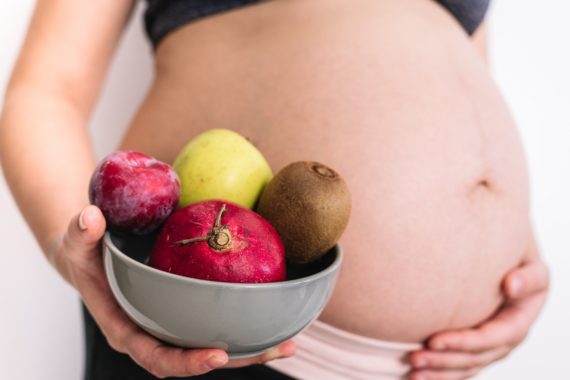 Pregnant woman holding a bowl of fruit in her hands. Healthy food concept during pregnancy.