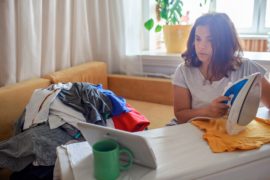Tired mom watches video on tablet and ironing things, next to her son with smartphone too